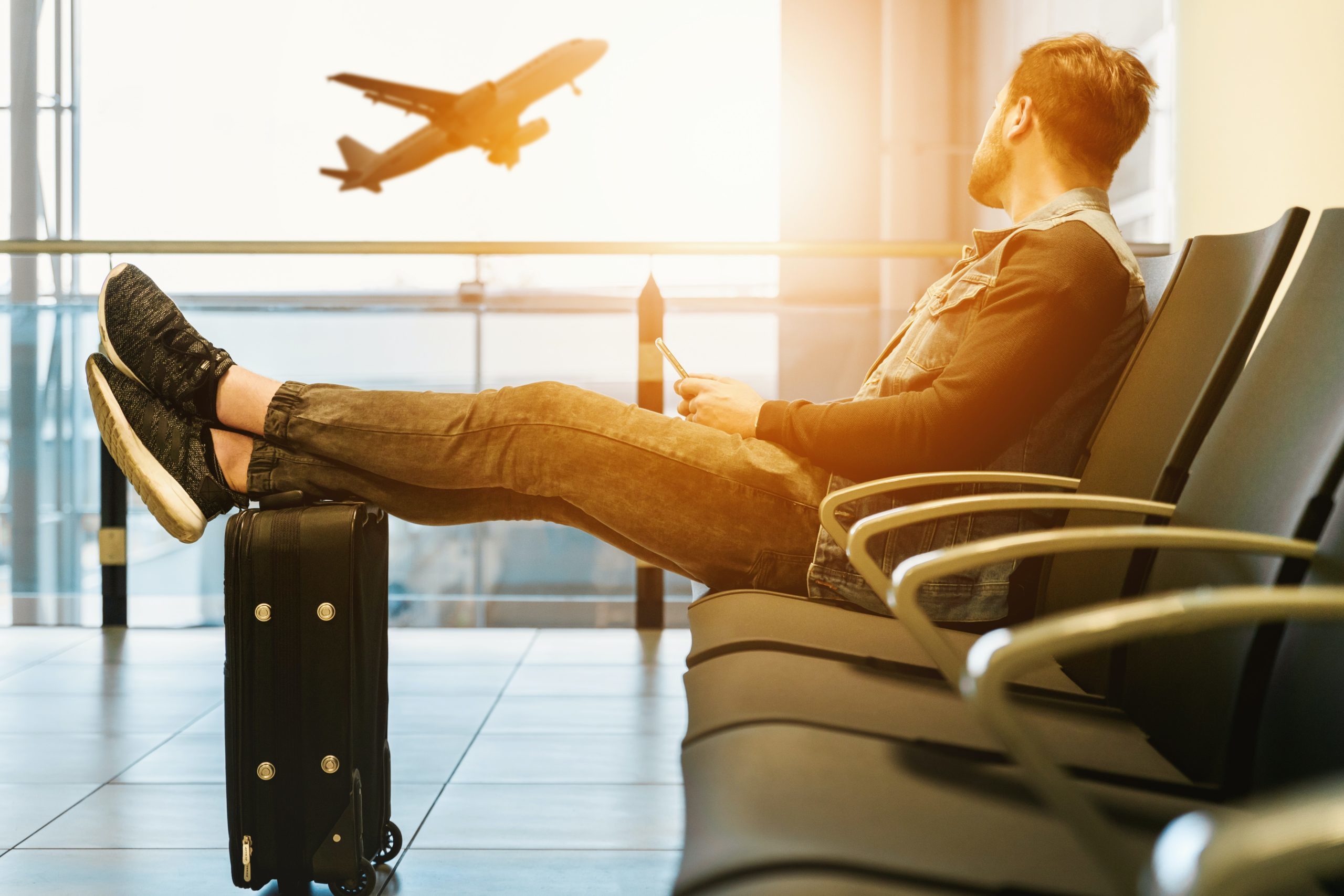 Man relaxing at an airport with legs on a suitcase while an airplane departs